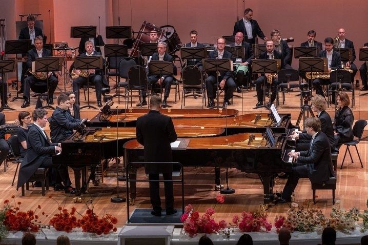 Junge Pianisten spielen an mehreren Flügeln vor einem Orchester